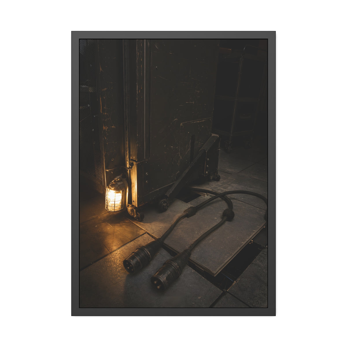 Two thick power cables unplugged on the floor beside a caged work lamp. The Redundant Power by Garabaggio, framed fine art print, 28″ x 40″.