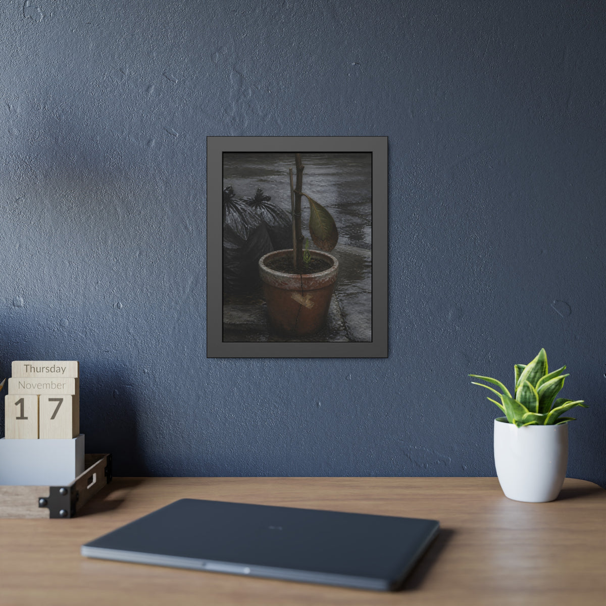 A taped clay pot with one leaf and a green shoot on wet pavement. The Green at the Base by Garabaggio, framed fine art print hanging in a room.