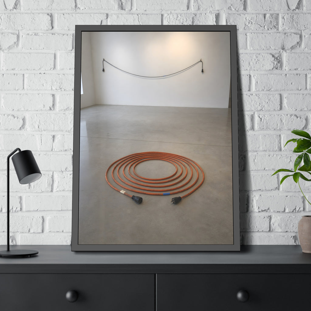 An orange extension cord coiled in a spiral on a bare gallery floor. The Floor Coil by Garabaggio, framed fine art print hanging in a room.