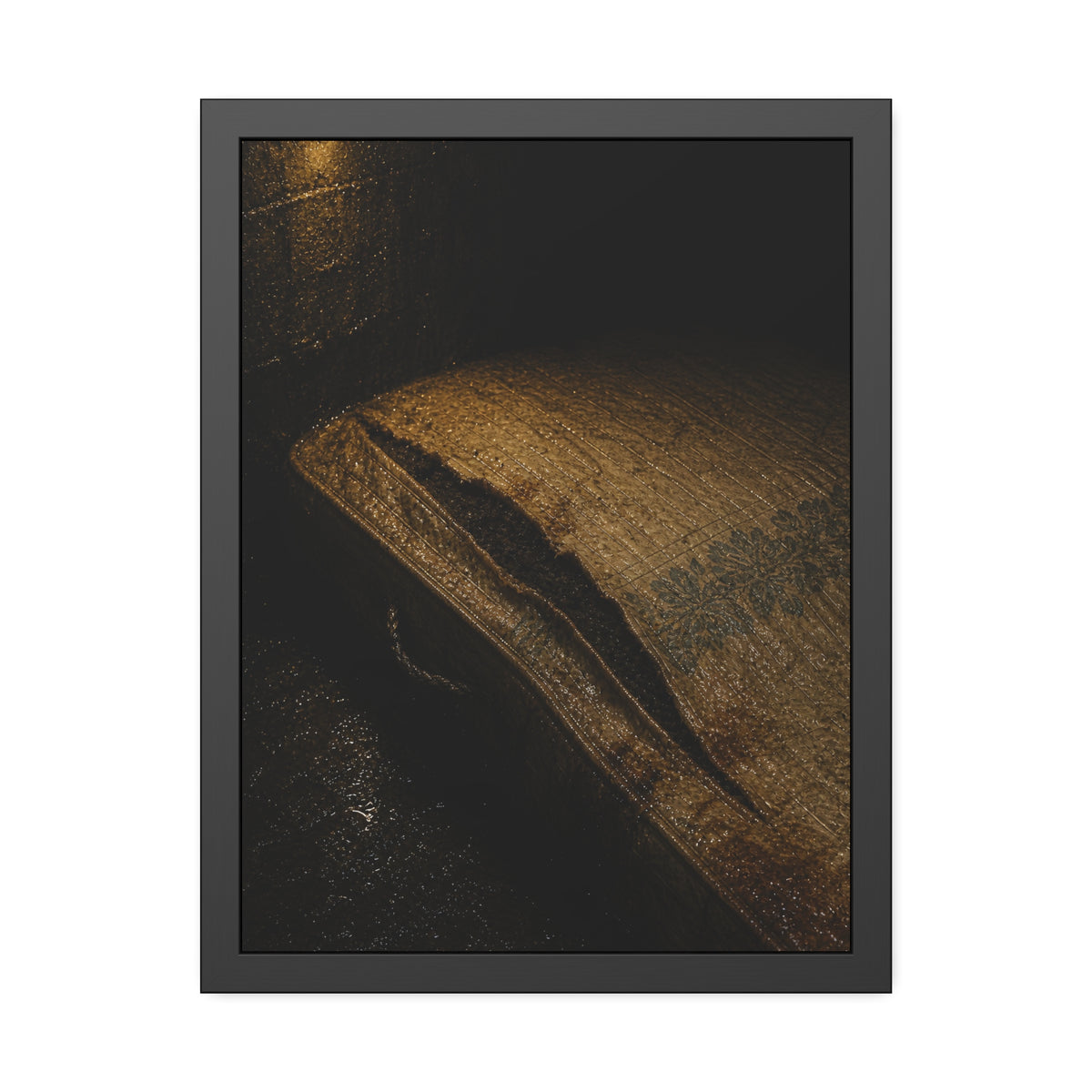 A mattress with its seam split open, lit warm against a dark wall. The Opening of the Ticking by Garabaggio, framed fine art print, 18″ x 24″.