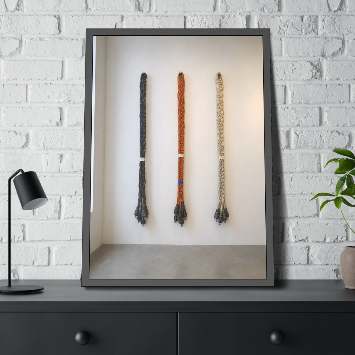 Three braided bundles of extension cords hung on a white gallery wall. The Braided Triptych by Garabaggio, framed fine art print hanging in a room.