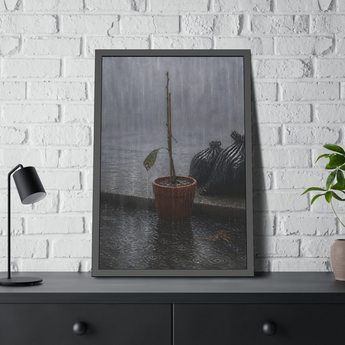 A bare stick in a clay pot on a curb in heavy rain beside trash bags. The Second Rain by Garabaggio, framed fine art print hanging in a room.