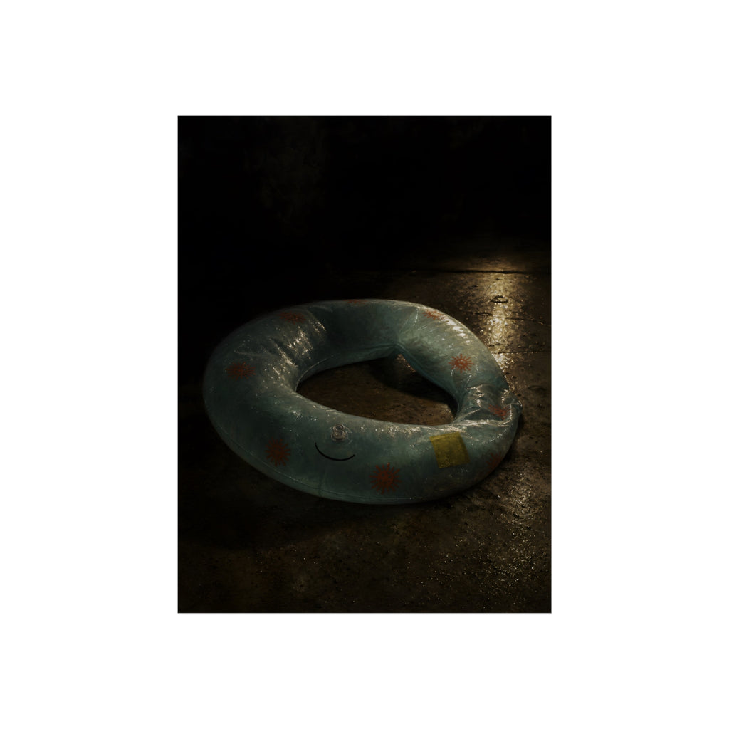 Deflated pool float ring on wet ground, lit from one side in the dark. After the Last Swim by Garabaggio, fine art print, 12″ x 16″.