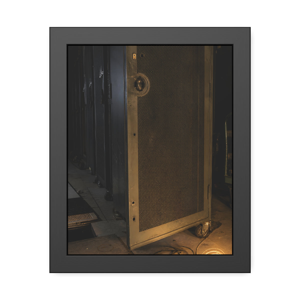 A perforated server rack door in a dark aisle lit by a floor work lamp. The Cold Aisle by Garabaggio, framed fine art print, 11″ x 14″.