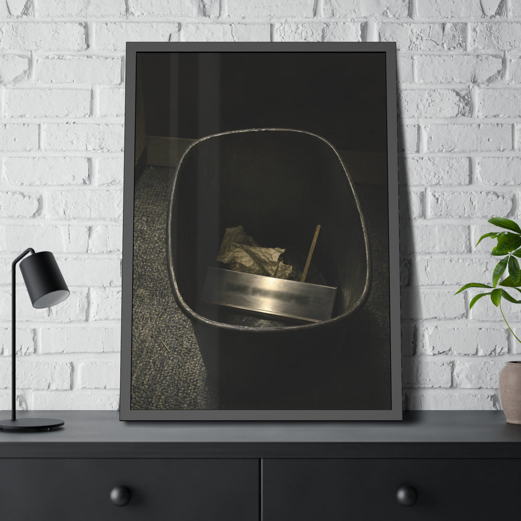 A metal nameplate lying in a black office waste bin on grey carpet. The Nameplate in the Waste Bin by Garabaggio, framed fine art print hanging in a room.