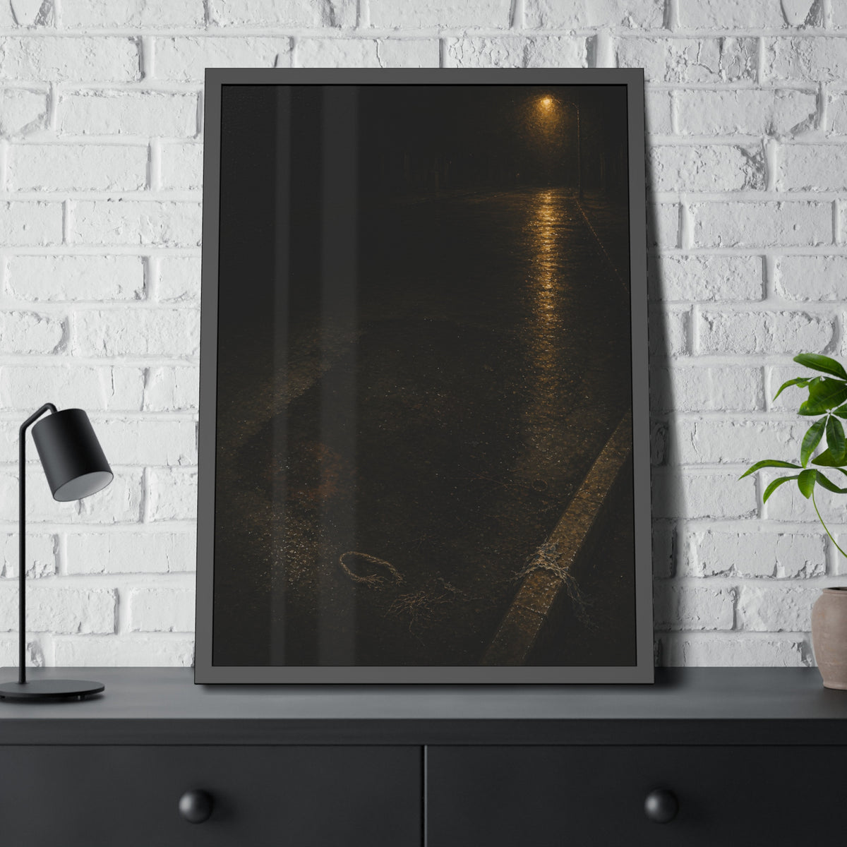 A rectangular stain on wet asphalt where something lay, under a streetlamp. The Stain After Removal by Garabaggio, framed fine art print hanging in a room.