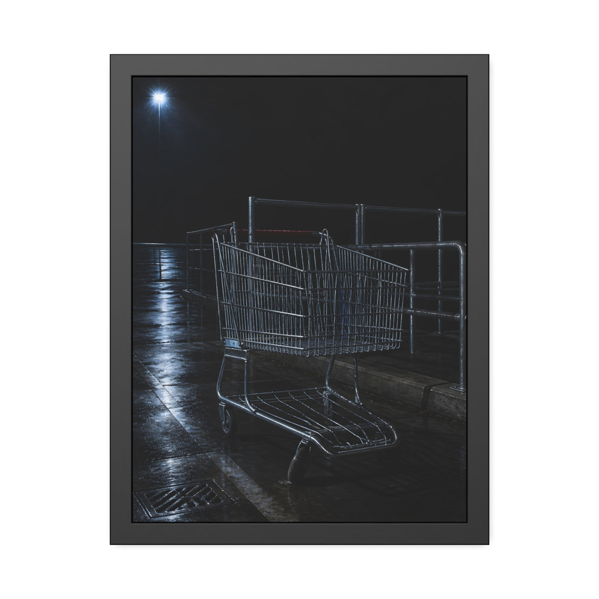 A shopping cart beside its corral on wet asphalt under a lot light. The Cart at the Corral by Garabaggio, framed fine art print, 18″ x 24″.
