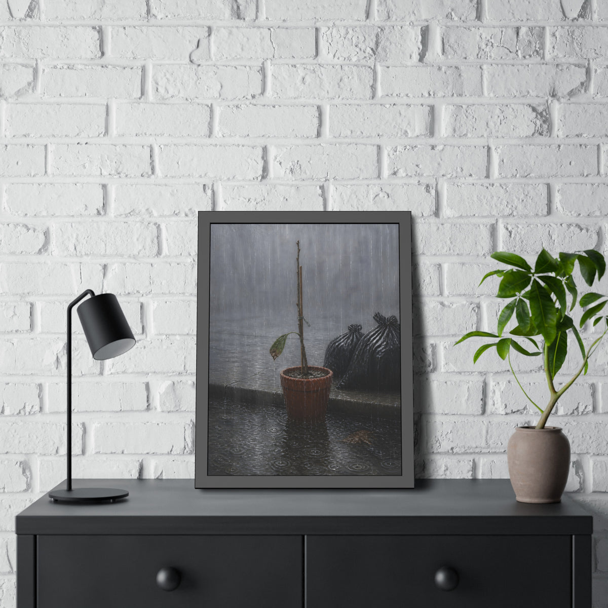 A bare stick in a clay pot on a curb in heavy rain beside trash bags. The Second Rain by Garabaggio, framed fine art print hanging in a room.