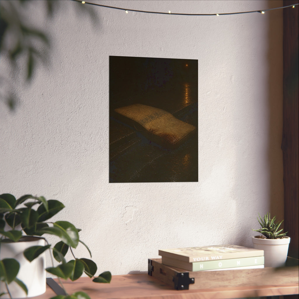 A sodden mattress slumped off a curb on wet pavement under a street lamp. The Collapse into the Gutter by Garabaggio, fine art print hanging in a room.