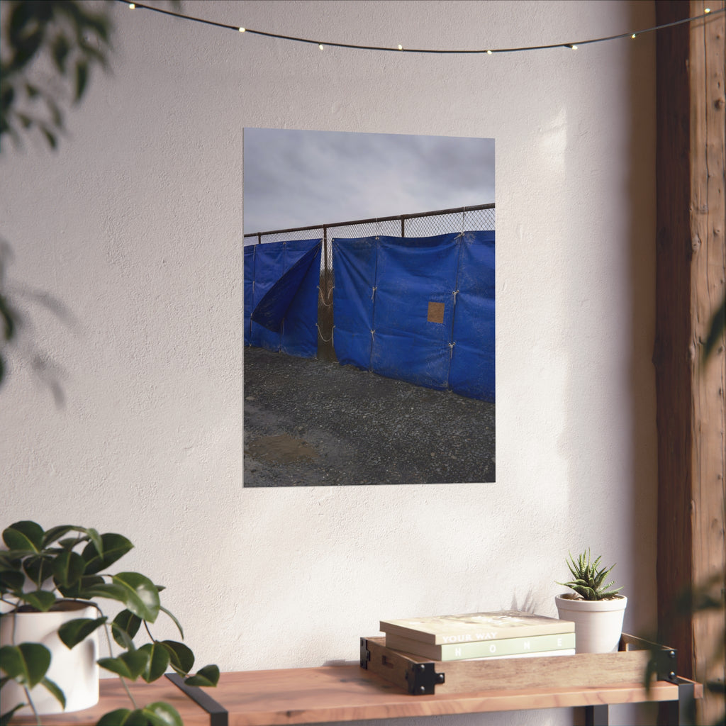 Blue tarps lashed to a chain link fence above gravel under grey sky. Drapery on the Fence by Garabaggio, fine art print hanging in a room.