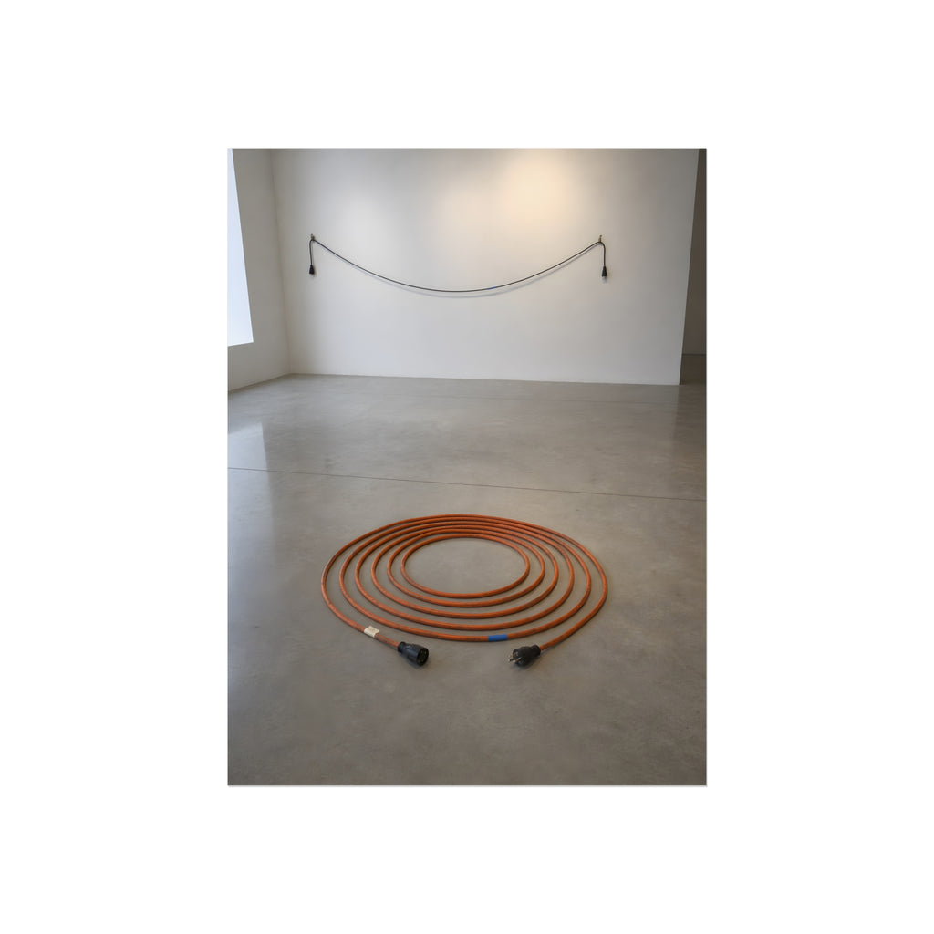 An orange extension cord coiled in a spiral on a bare gallery floor. The Floor Coil by Garabaggio, fine art print, 12″ x 16″.