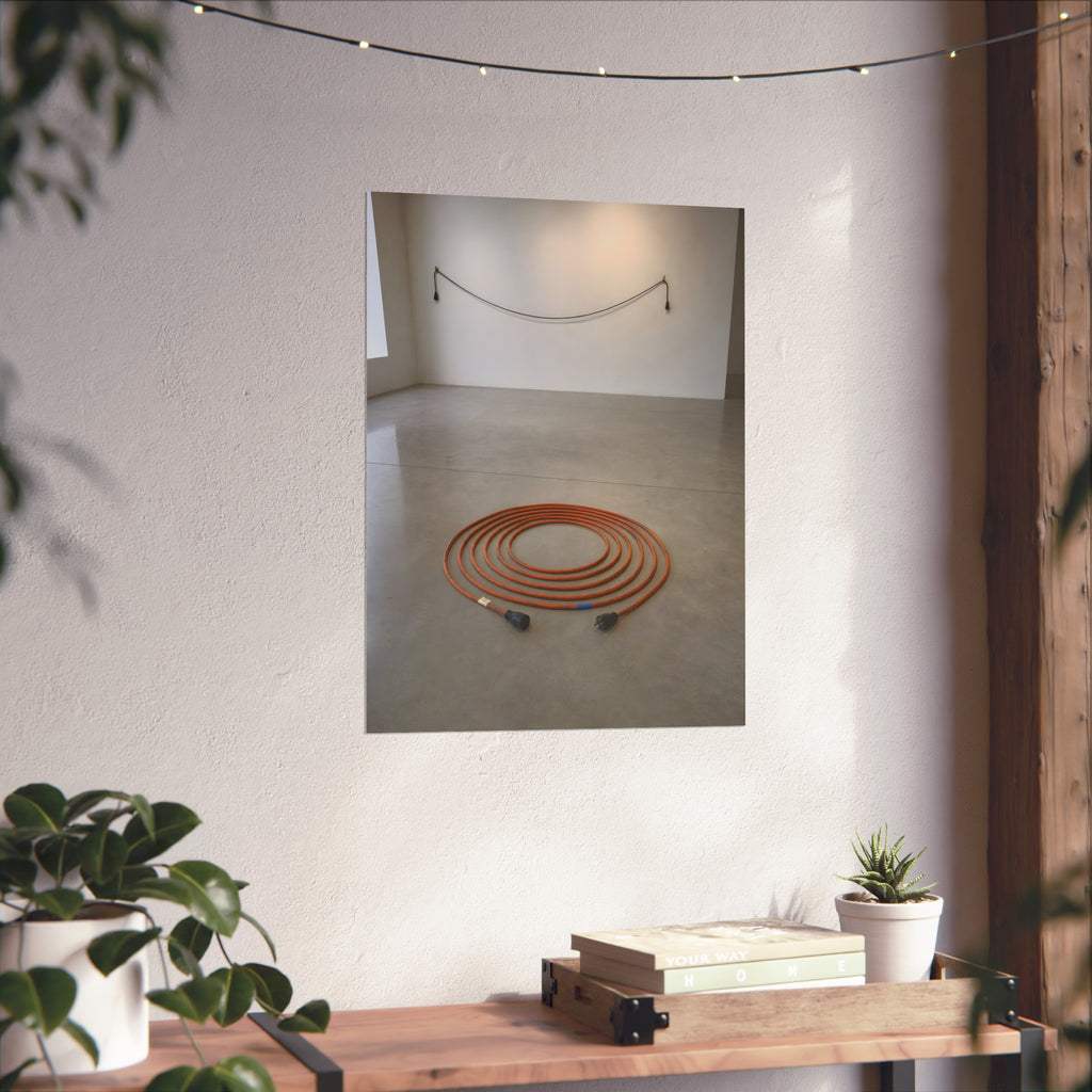 An orange extension cord coiled in a spiral on a bare gallery floor. The Floor Coil by Garabaggio, fine art print hanging in a room.