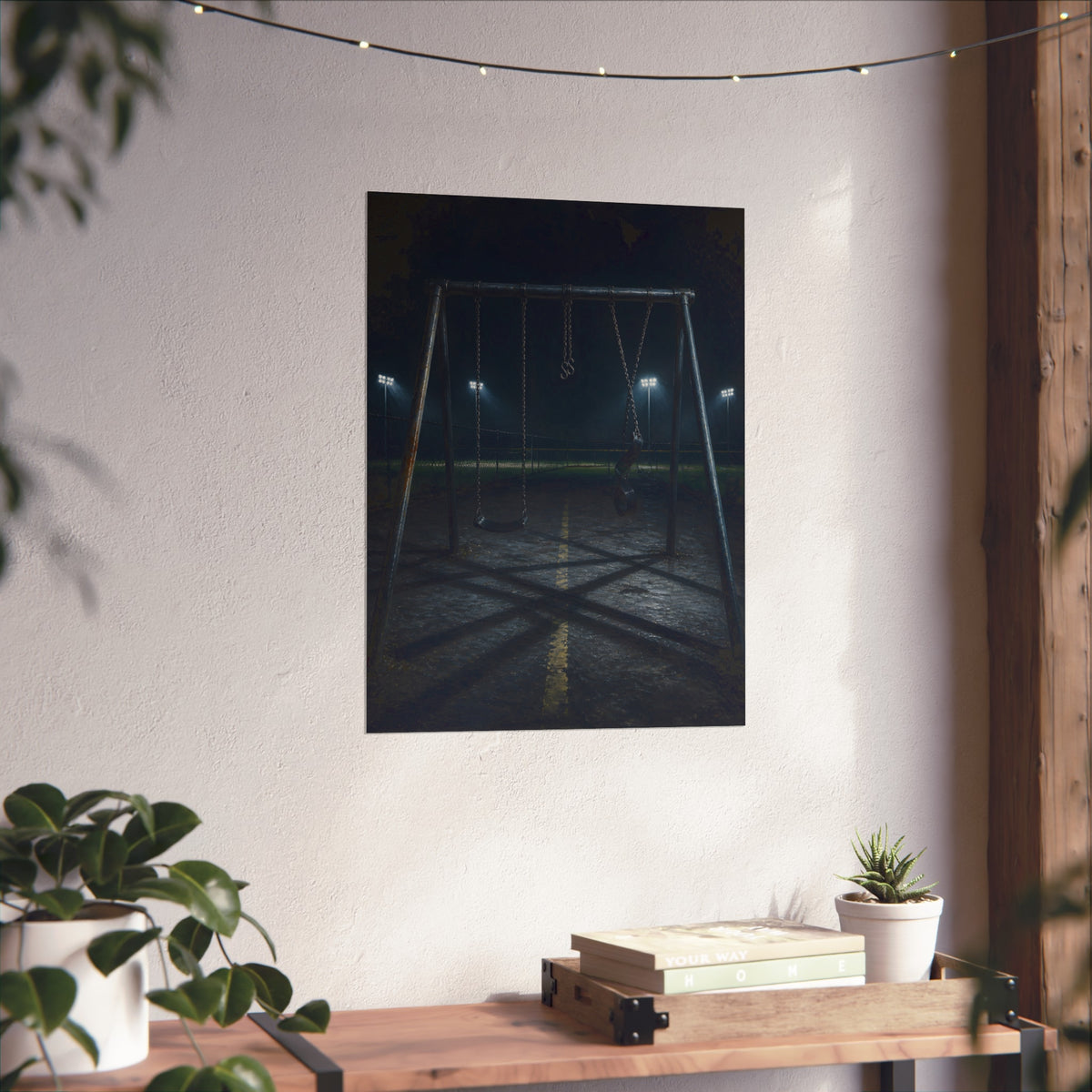 An empty swing set at night with field lights glowing behind it. The Ninth Hour: The Seat Still Moving by Garabaggio, fine art print hanging in a room.