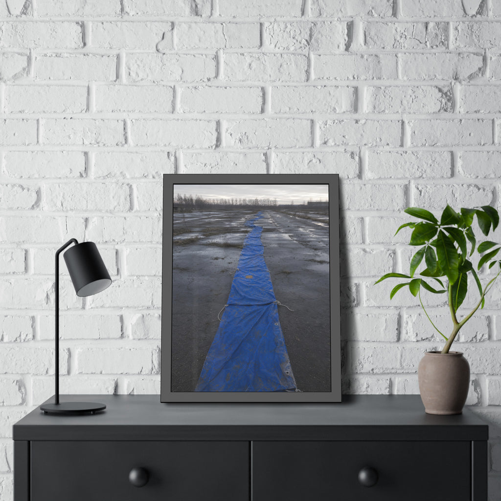 A blue tarp laid in a long strip down a wet cracked lot under grey sky. The Long Ground Procession by Garabaggio, framed fine art print hanging in a room.