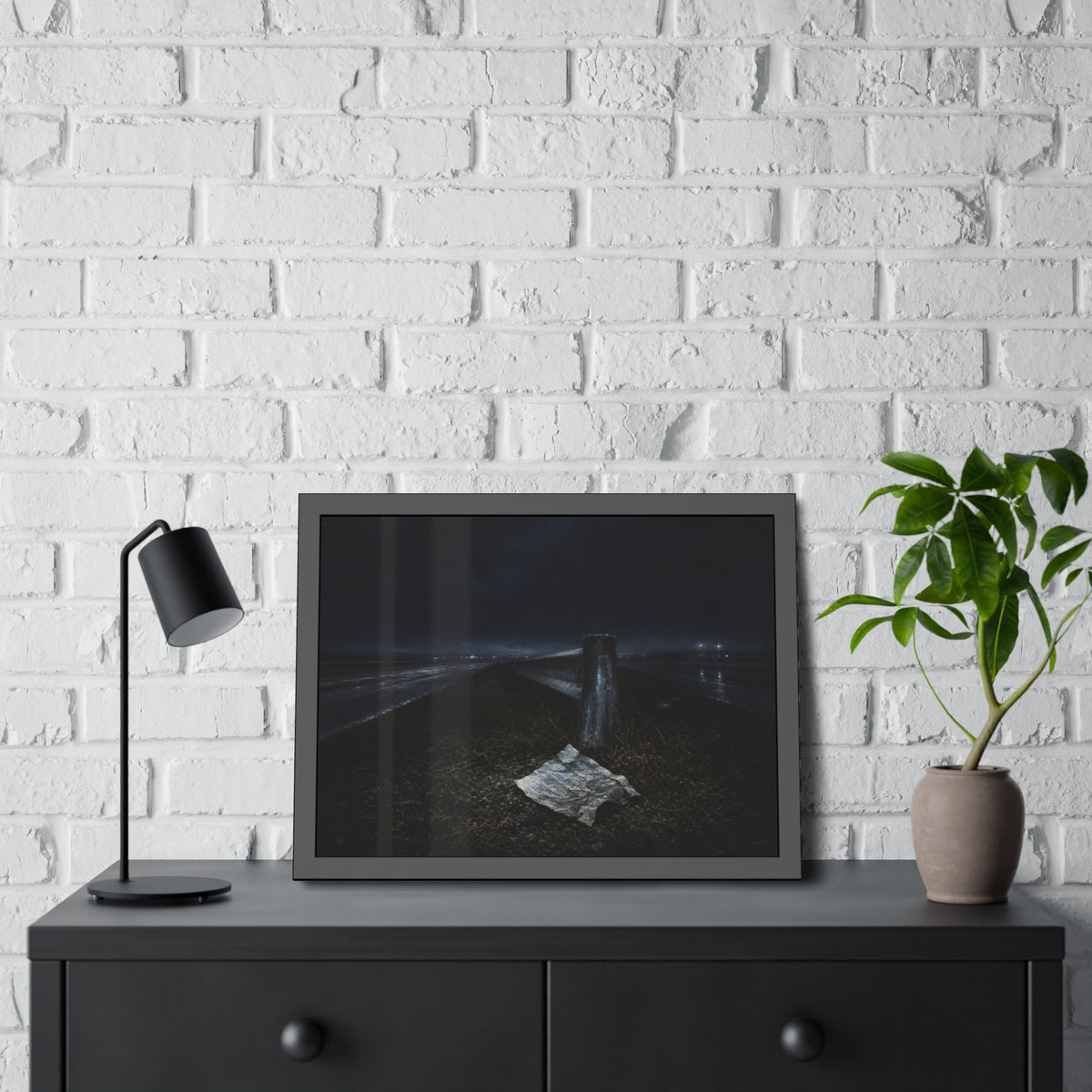 A sheet of paper on a grassy highway median beside a concrete post at night. The Resume on the Median by Garabaggio, framed fine art print hanging in a room.