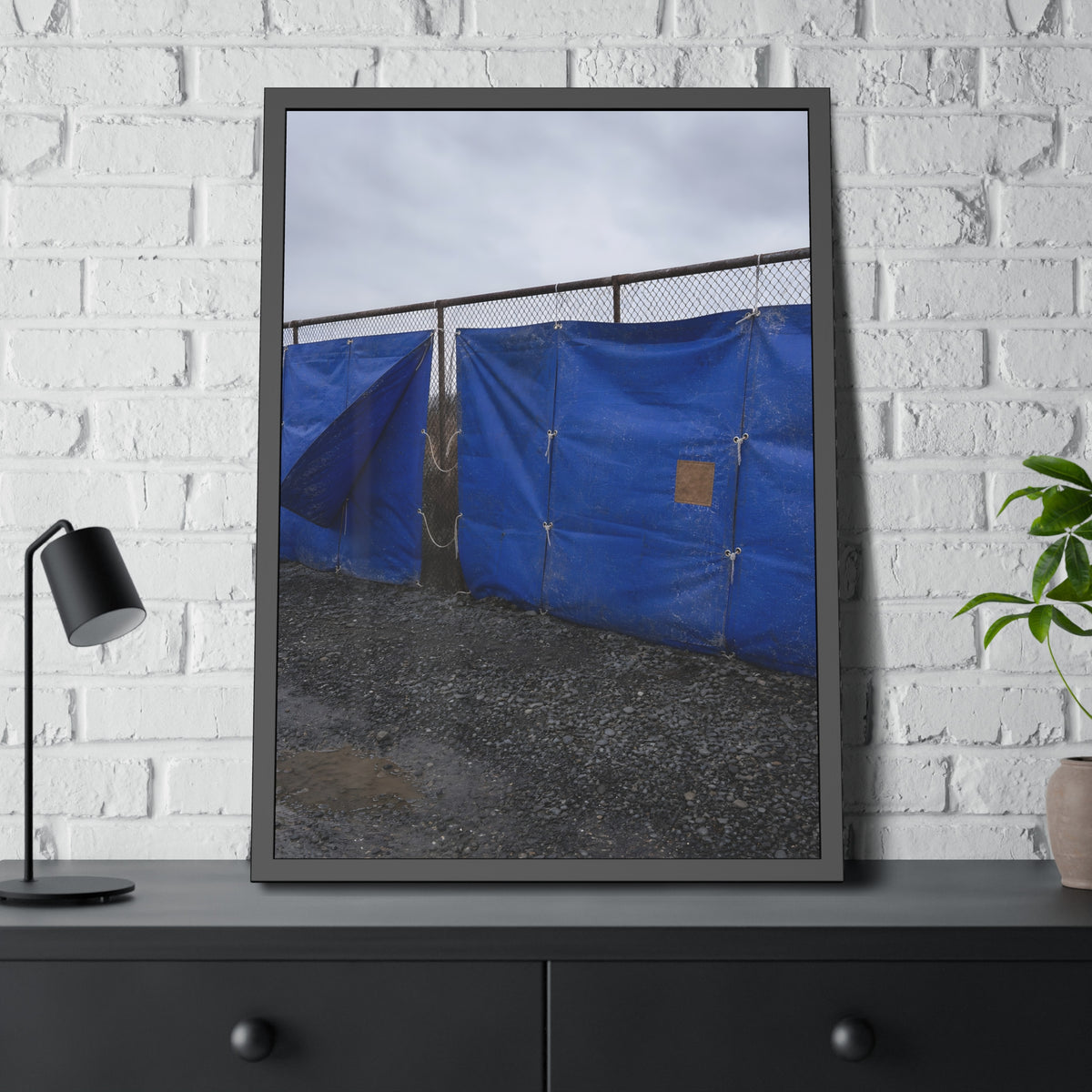 Blue tarps lashed to a chain link fence above gravel under grey sky. Drapery on the Fence by Garabaggio, framed fine art print hanging in a room.