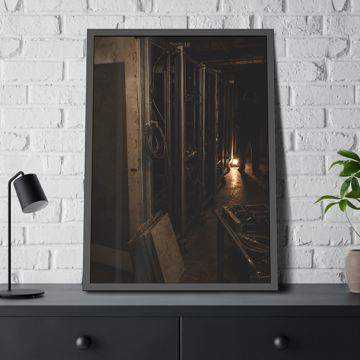 Open server racks in a dark room, a work lamp and a figure at the end. Garabaggio at the End of the Row by Garabaggio, framed fine art print hanging in a room.