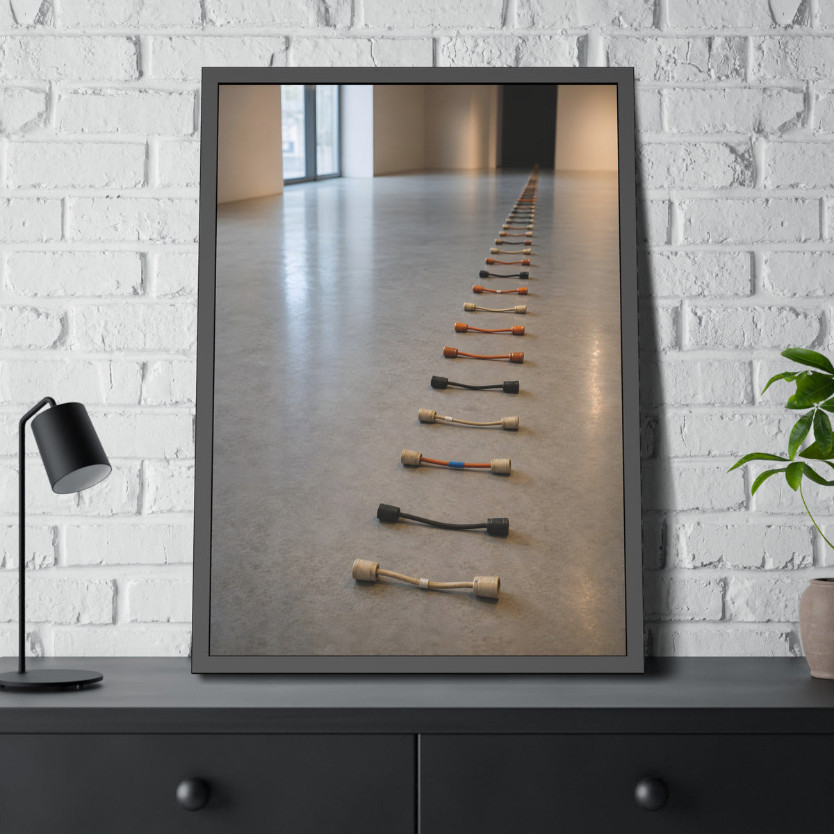A long line of cut extension cord ends laid across a pale gallery floor. The Severed Procession by Garabaggio, framed fine art print hanging in a room.
