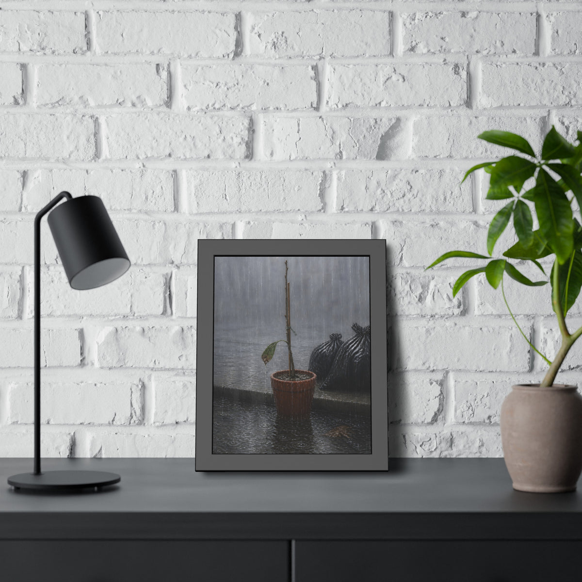 A bare stick in a clay pot on a curb in heavy rain beside trash bags. The Second Rain by Garabaggio, framed fine art print hanging in a room.