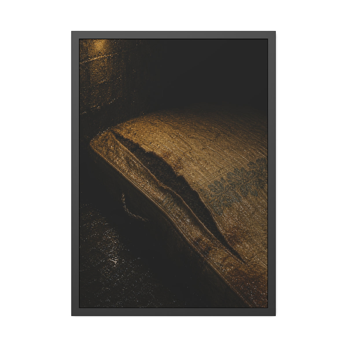 A mattress with its seam split open, lit warm against a dark wall. The Opening of the Ticking by Garabaggio, framed fine art print, 28″ x 40″.