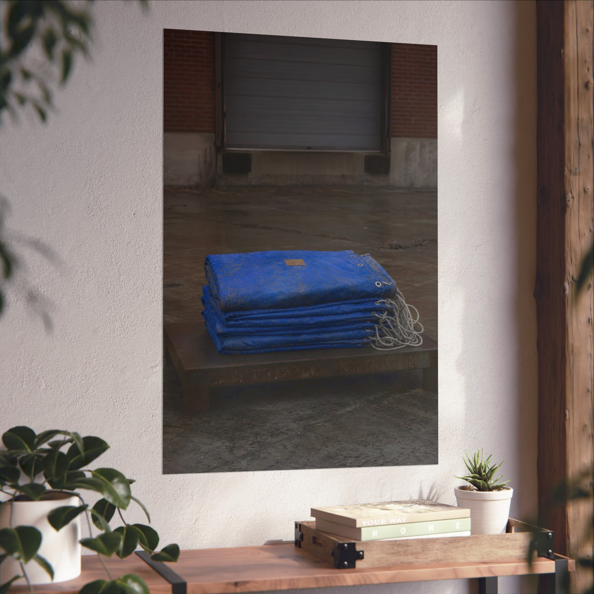 A folded blue tarp stacked on a low wooden platform by a loading dock. The Repaired Fold by Garabaggio, fine art print hanging in a room.
