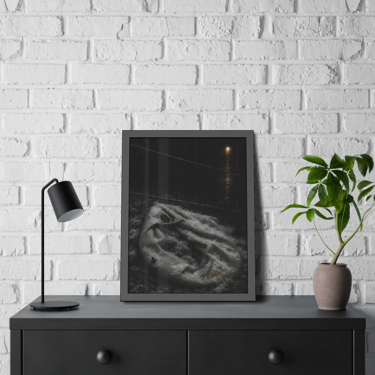 A deflated pool float under snow beside a chain link fence at night. The Bleaching Under Snow by Garabaggio, framed fine art print hanging in a room.