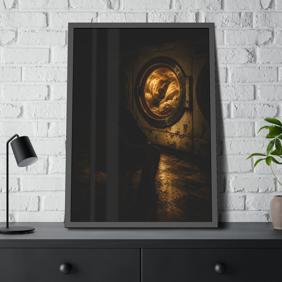A person seated in a plastic chair facing a lit dryer drum. The Watcher in the Plastic Chair by Garabaggio, framed fine art print hanging in a room.