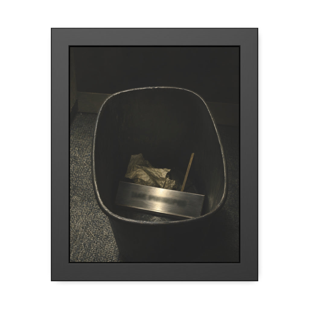 A metal nameplate lying in a black office waste bin on grey carpet. The Nameplate in the Waste Bin by Garabaggio, framed fine art print, 11″ x 14″.