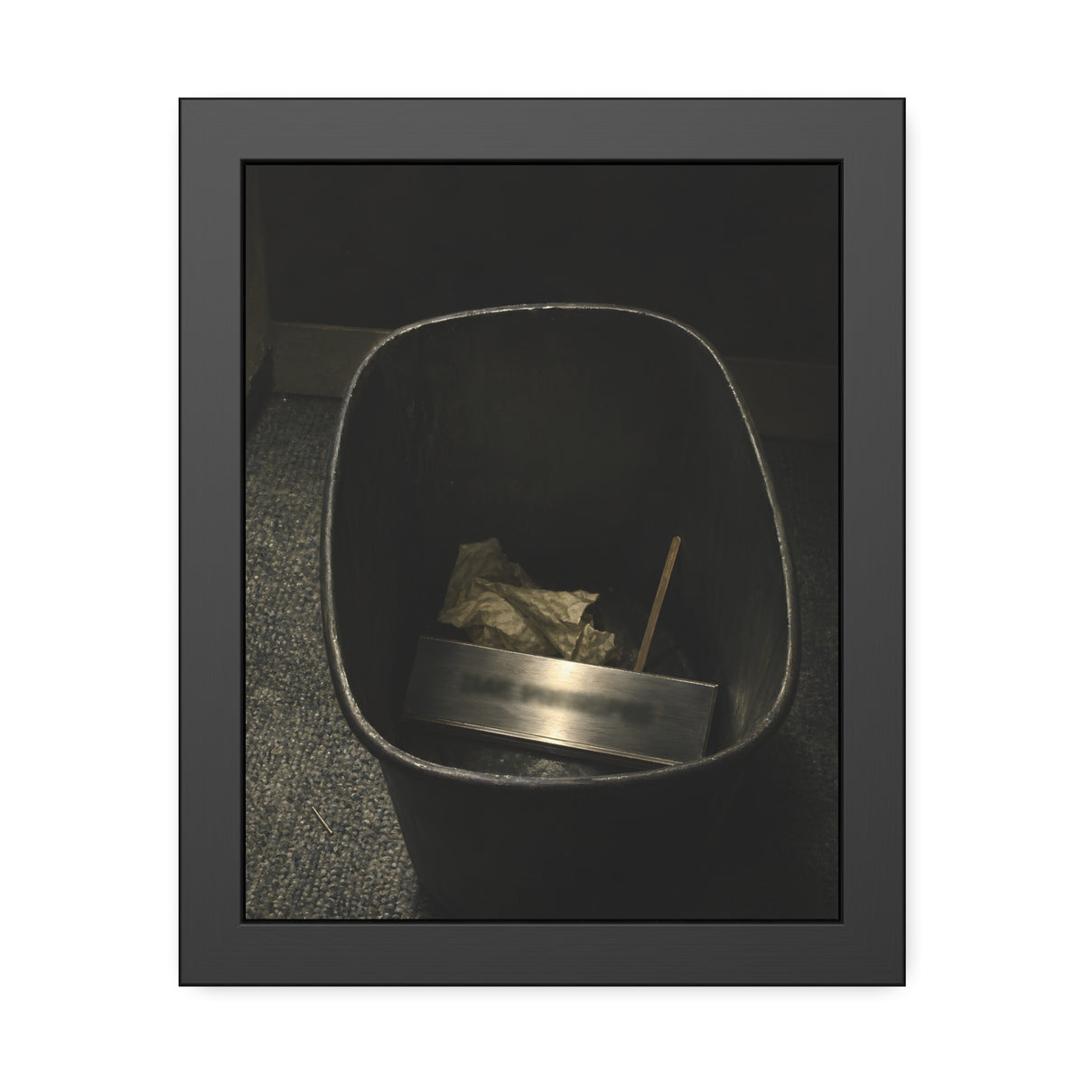 A metal nameplate lying in a black office waste bin on grey carpet. The Nameplate in the Waste Bin by Garabaggio, framed fine art print, 11″ x 14″.