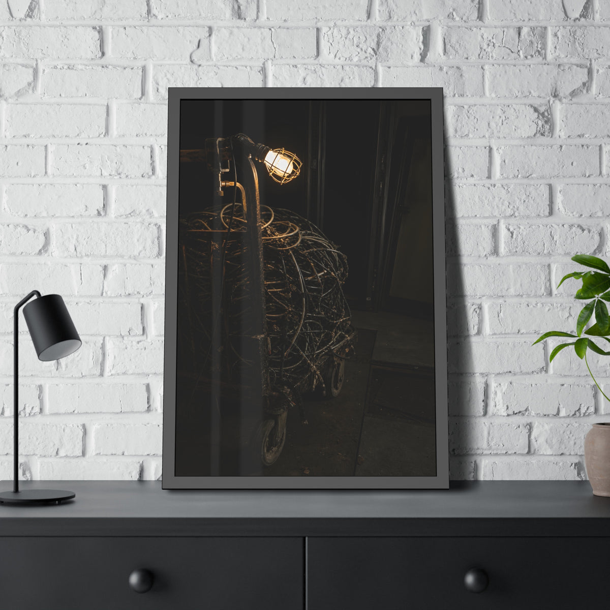 A tangled ball of cables on a hand cart under a caged work lamp. The Cable Harvest by Garabaggio, framed fine art print hanging in a room.