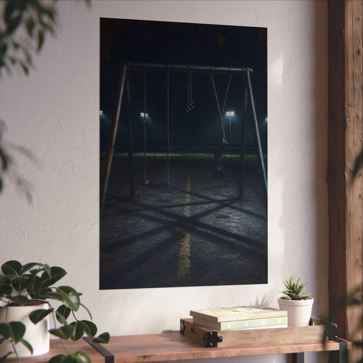 An empty swing set at night with field lights glowing behind it. The Ninth Hour: The Seat Still Moving by Garabaggio, fine art print hanging in a room.