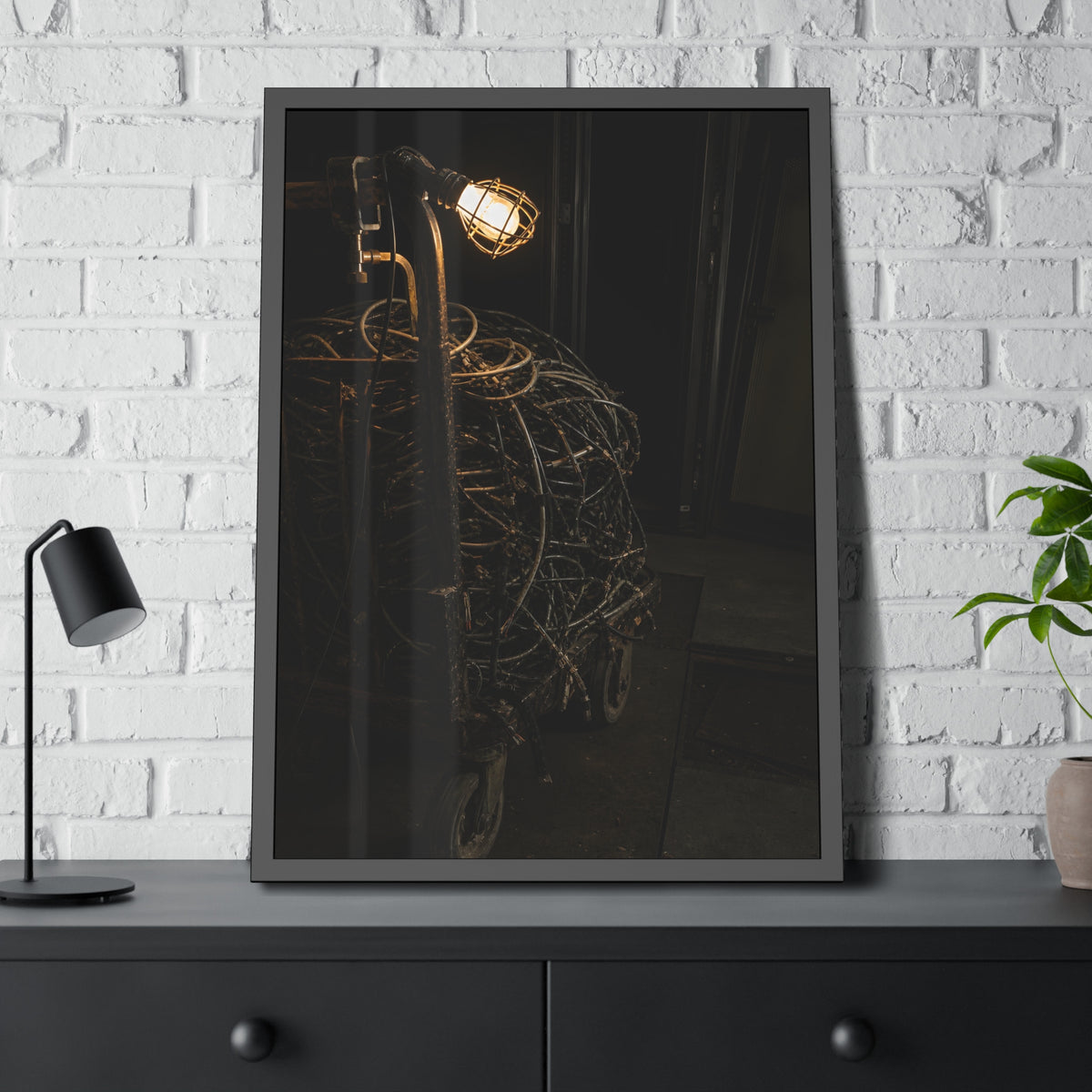 A tangled ball of cables on a hand cart under a caged work lamp. The Cable Harvest by Garabaggio, framed fine art print hanging in a room.