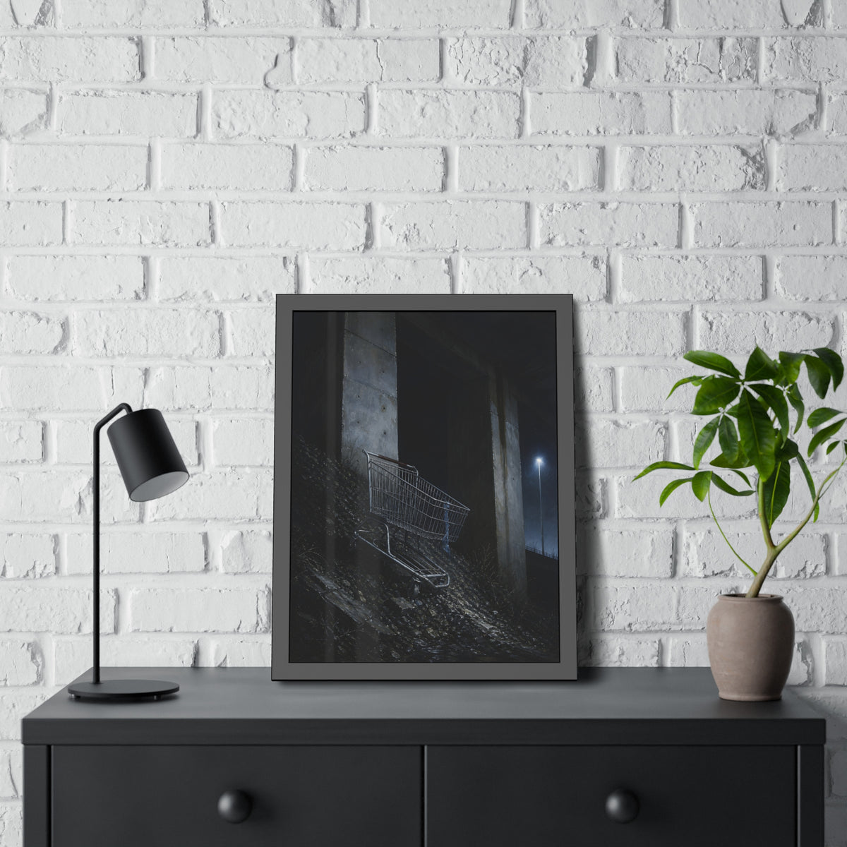 A shopping cart on a rocky slope under an overpass near a streetlamp. The Descent to the Underpass by Garabaggio, framed fine art print hanging in a room.