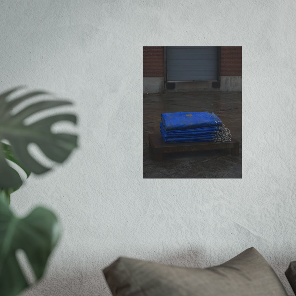 A folded blue tarp stacked on a low wooden platform by a loading dock. The Repaired Fold by Garabaggio, fine art print hanging in a room.