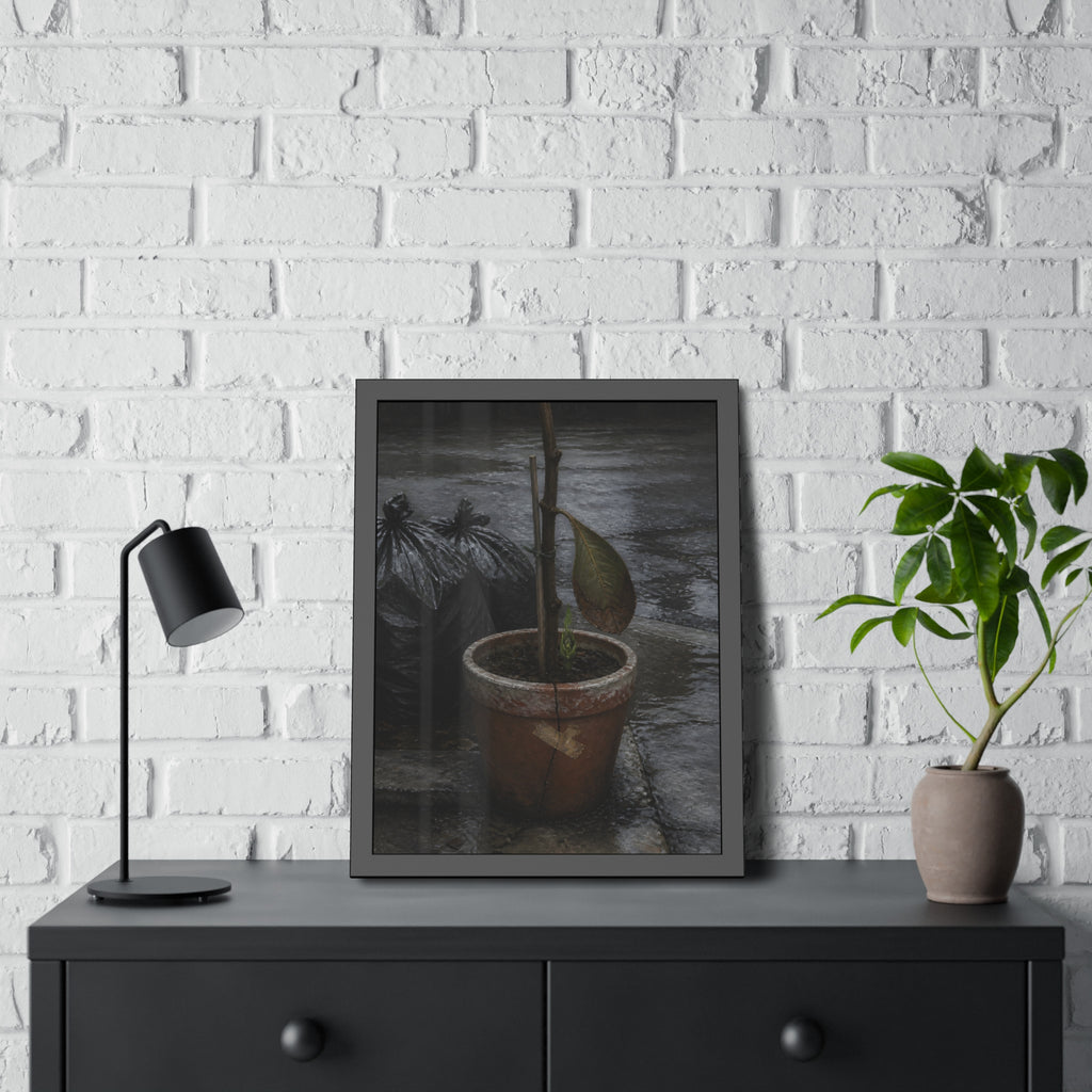 A taped clay pot with one leaf and a green shoot on wet pavement. The Green at the Base by Garabaggio, framed fine art print hanging in a room.