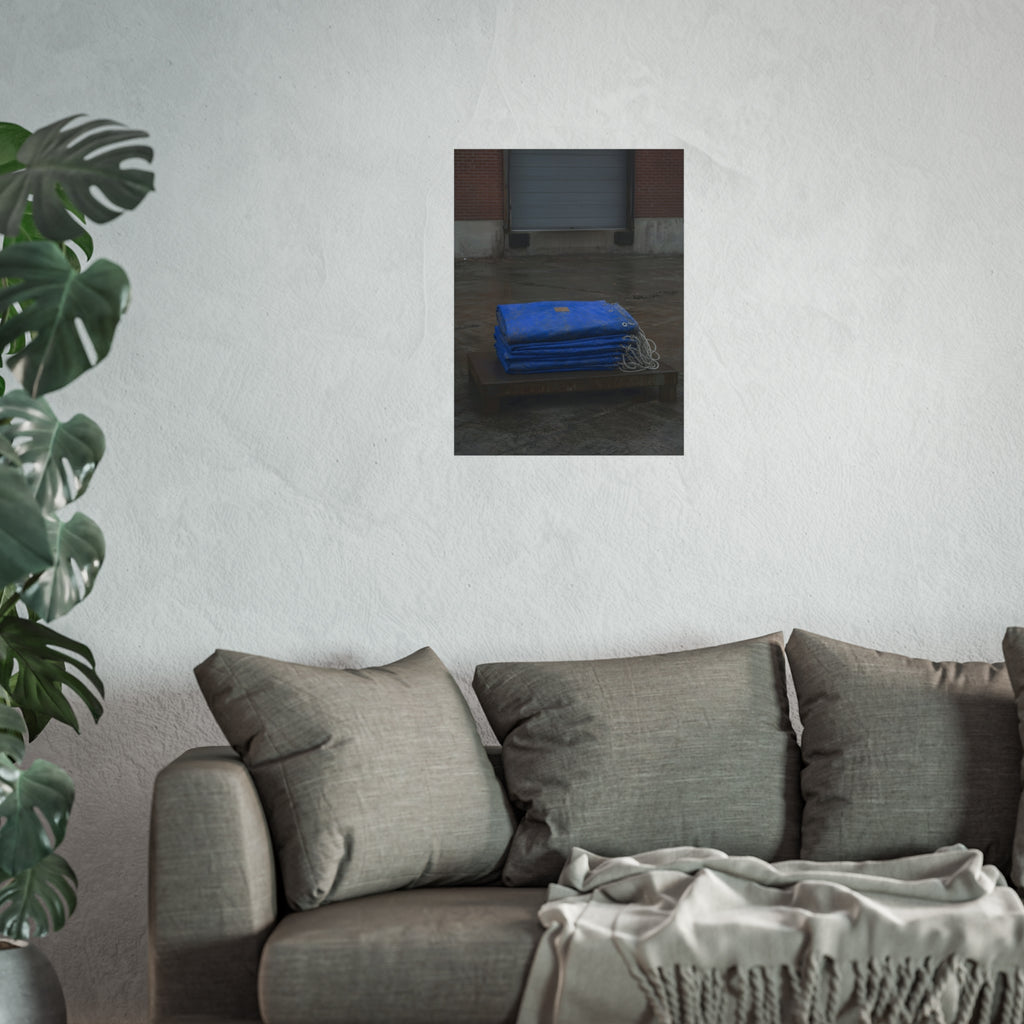 A folded blue tarp stacked on a low wooden platform by a loading dock. The Repaired Fold by Garabaggio, fine art print hanging in a room.
