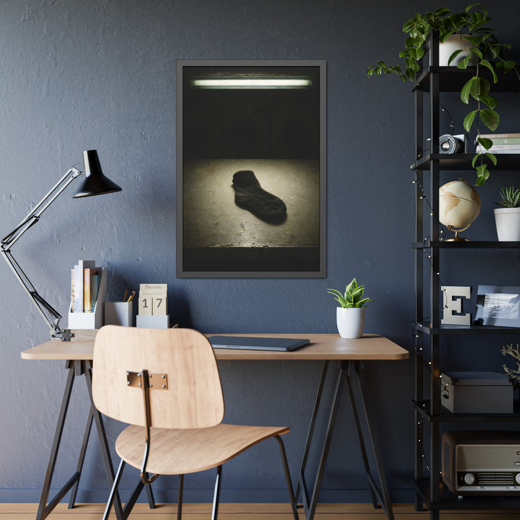 A single dark sock on a laundromat floor before dim washing machines. The Orphaned Sock by Garabaggio, framed fine art print hanging in a room.