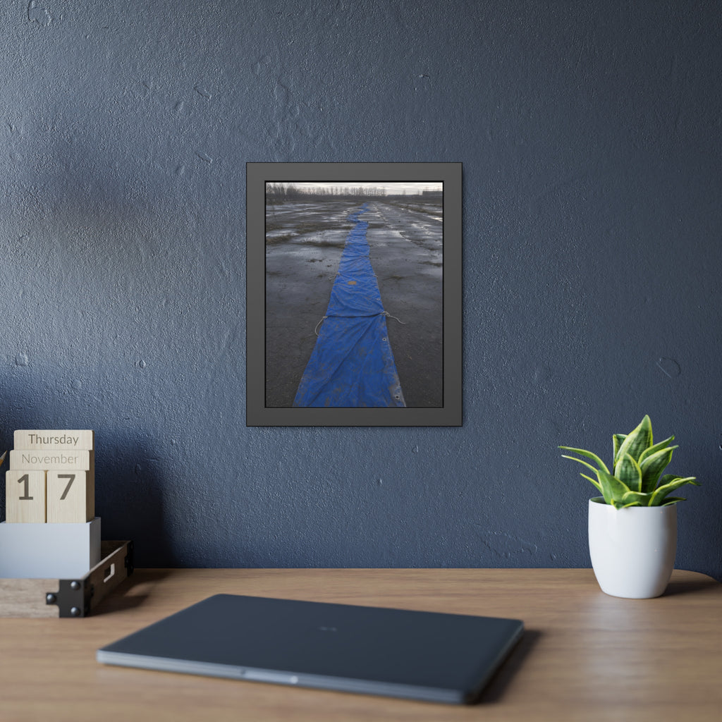 A blue tarp laid in a long strip down a wet cracked lot under grey sky. The Long Ground Procession by Garabaggio, framed fine art print hanging in a room.