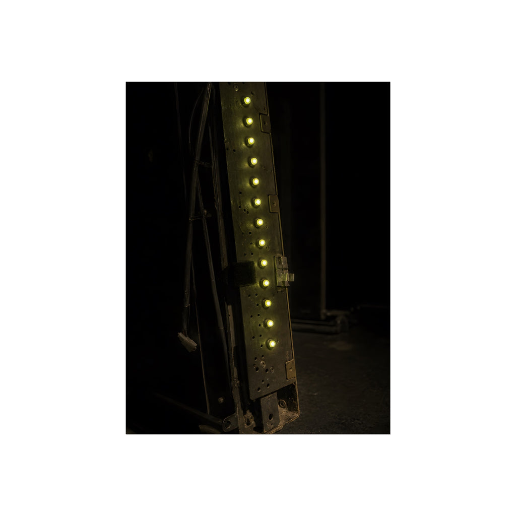 A dark rack panel with a vertical row of glowing green indicator lights. The First Green Choir by Garabaggio, fine art print, 12″ x 16″.