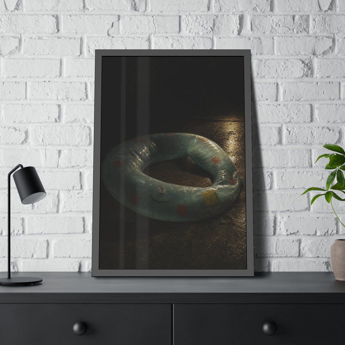 Deflated pool float ring on wet ground, lit from one side in the dark. After the Last Swim by Garabaggio, framed fine art print hanging in a room.