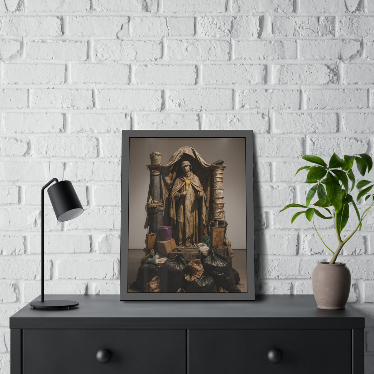 Draped standing figure under a canopy above a heap of black garbage bags. Saint Francis of the Black Bag by Garabaggio, framed fine art print hanging in a room.