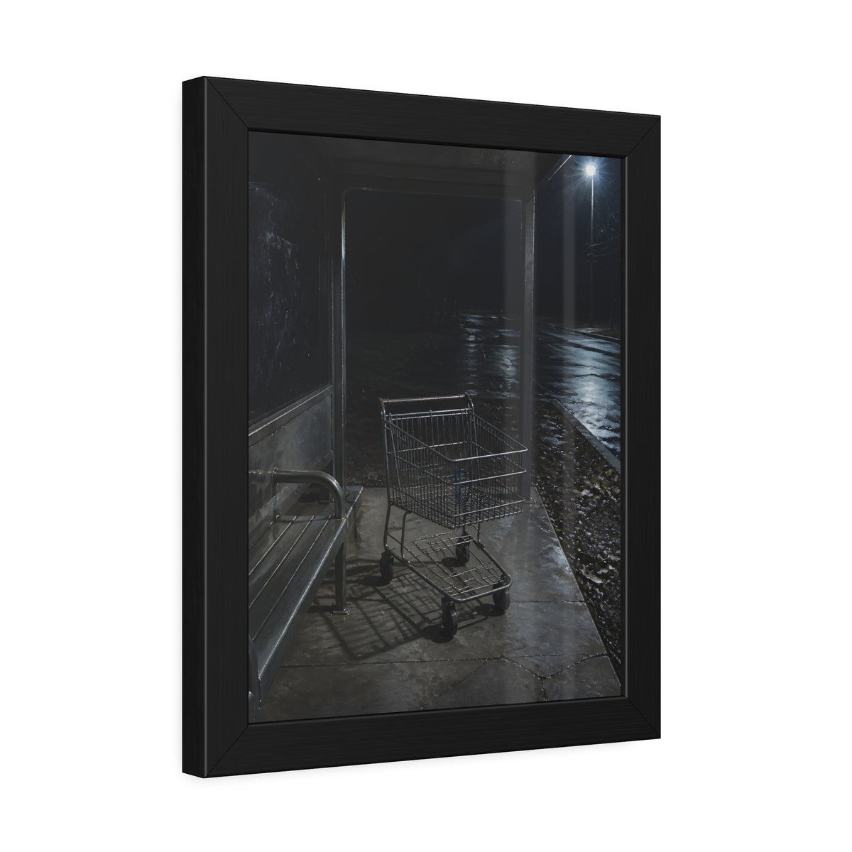 A shopping cart parked inside a bus shelter under a street lamp at night. The Rest at the Bus Shelter by Garabaggio, framed fine art print hanging in a room.