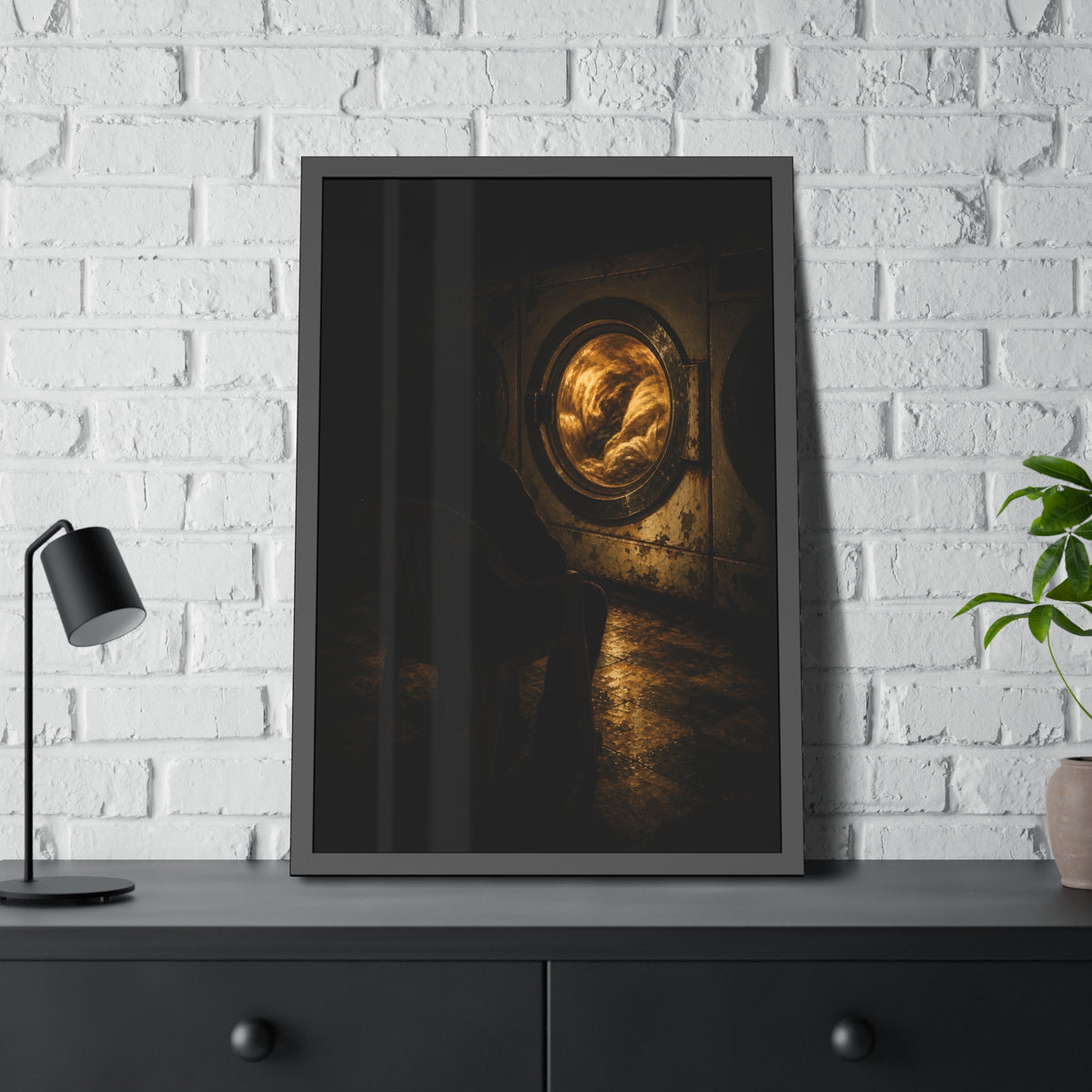 A person seated in a plastic chair facing a lit dryer drum. The Watcher in the Plastic Chair by Garabaggio, framed fine art print hanging in a room.
