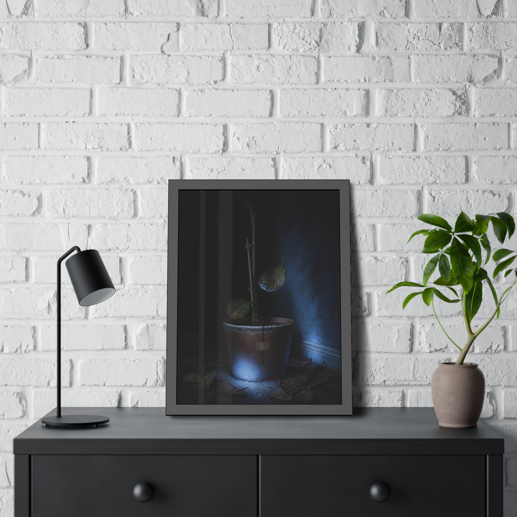 A bare potted plant dropping a leaf, dead leaves on the floor. The Leaf Lets Go by Garabaggio, framed fine art print hanging in a room.