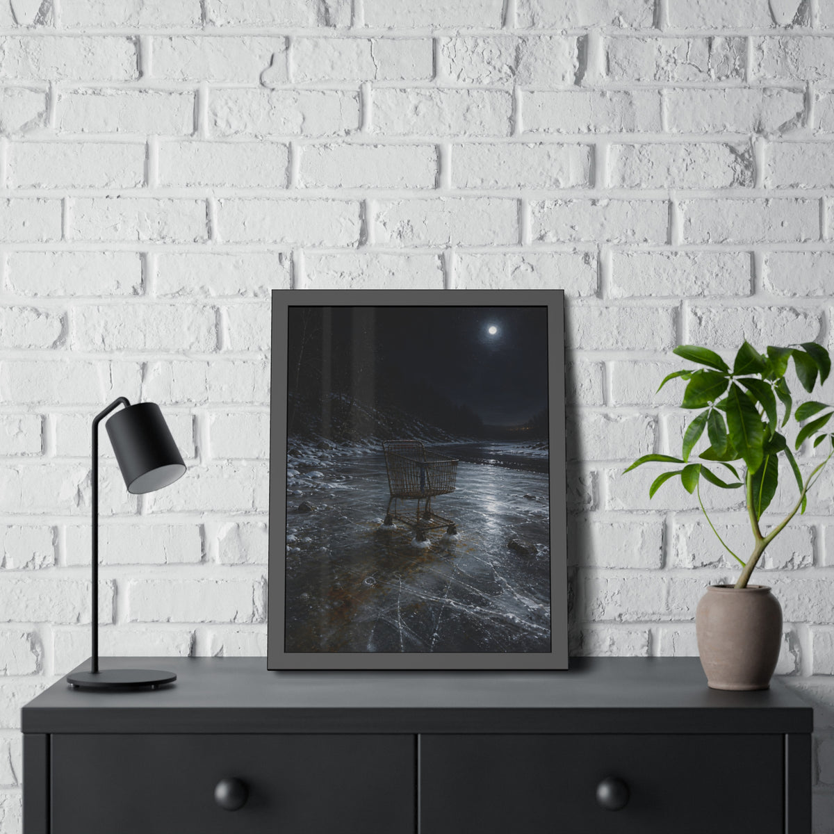 A rusted shopping cart frozen into moonlit river ice. The Wintering in the Ice by Garabaggio, framed fine art print hanging in a room.