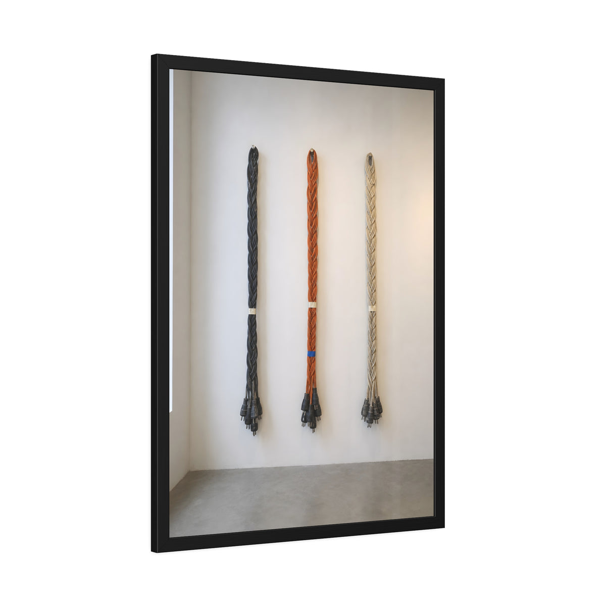 Three braided bundles of extension cords hung on a white gallery wall. The Braided Triptych by Garabaggio, framed fine art print hanging in a room.