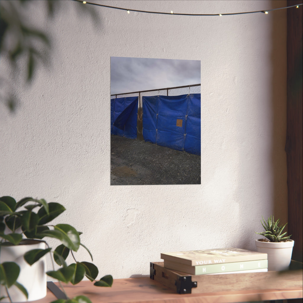 Blue tarps lashed to a chain link fence above gravel under grey sky. Drapery on the Fence by Garabaggio, fine art print hanging in a room.