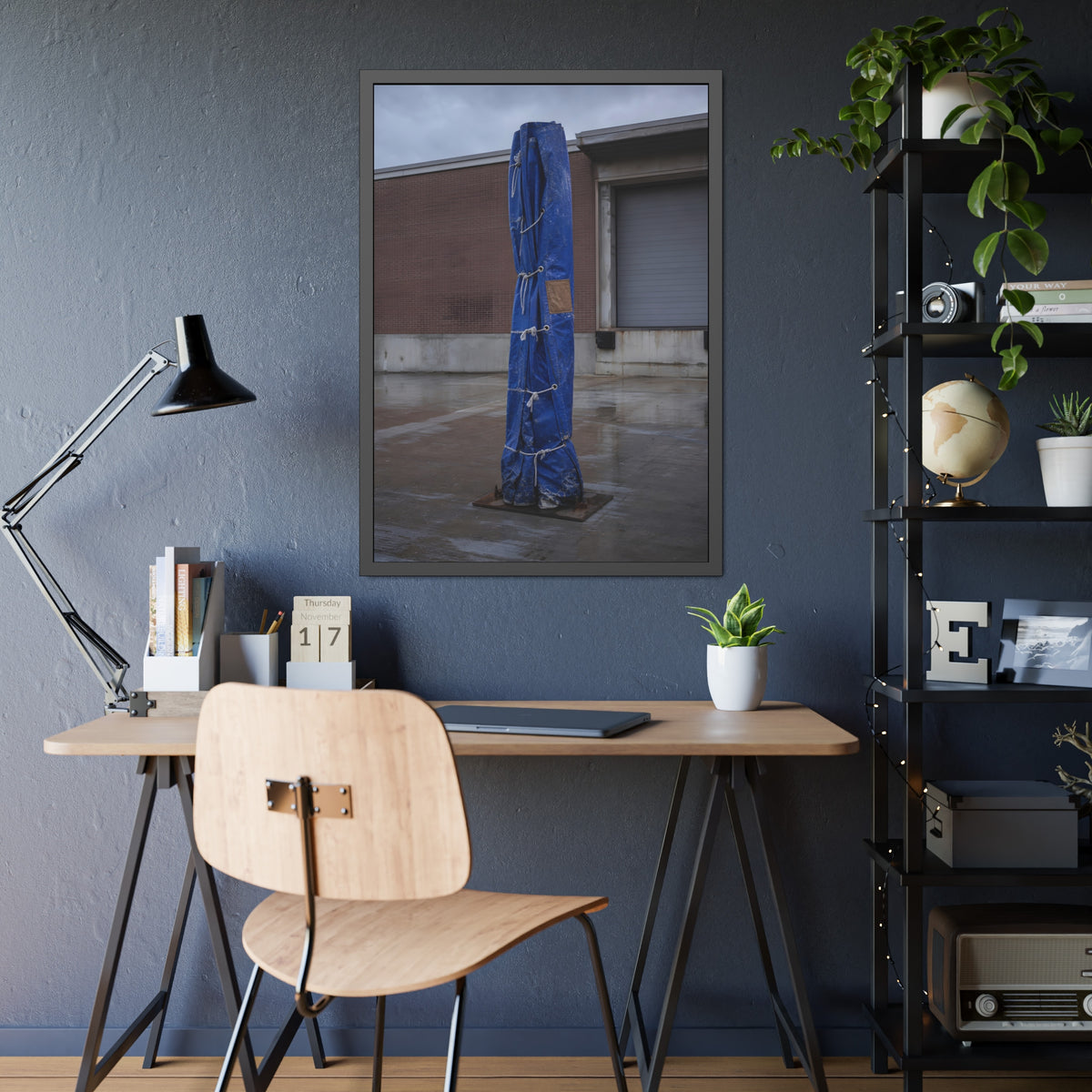A tall blue tarp bundle roped upright on a wet lot by a loading dock. Folded Standard at the Loading Bay by Garabaggio, framed fine art print hanging in a room.