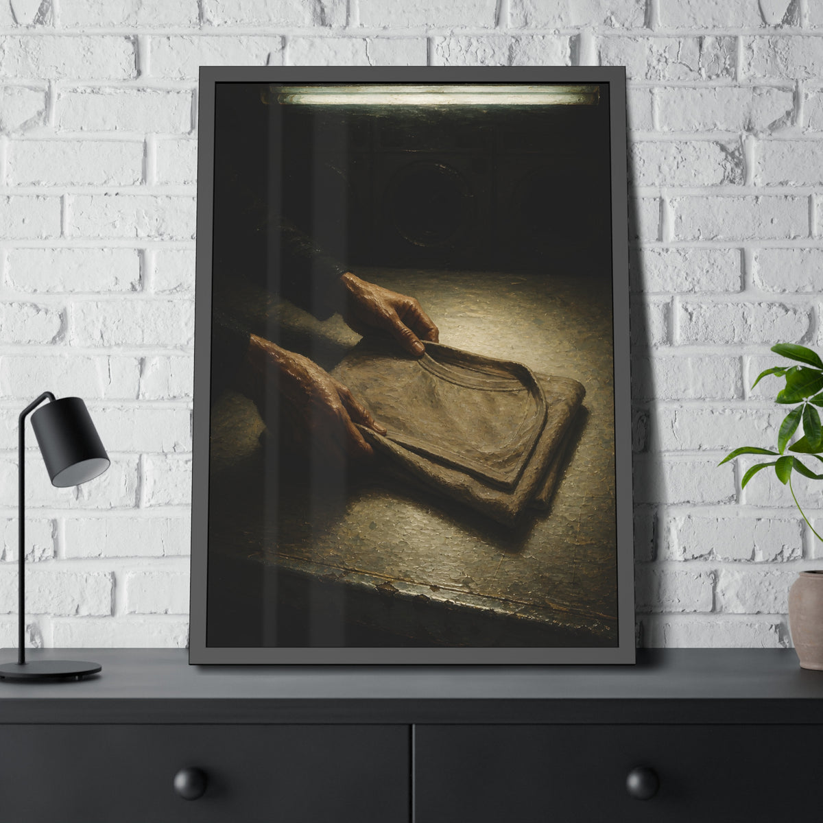 Two hands folding a shirt on a laundromat table with washers behind. The Folding at Two A.M by Garabaggio, framed fine art print hanging in a room.