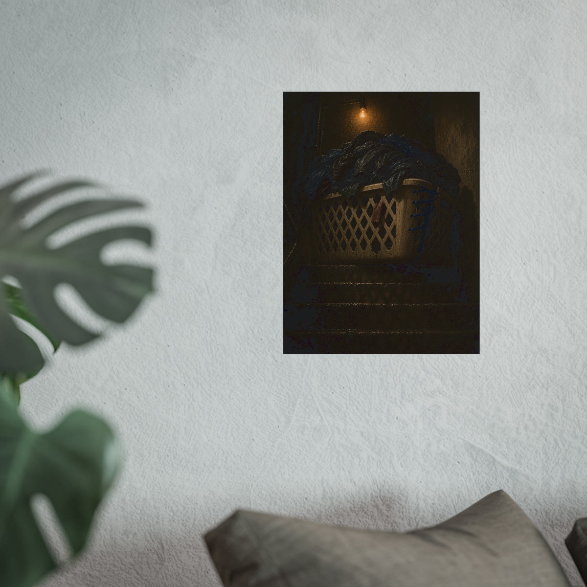 A laundry basket heaped with clothes on stairs under a bare bulb. The Overload on the Basement Stairs by Garabaggio, fine art print hanging in a room.